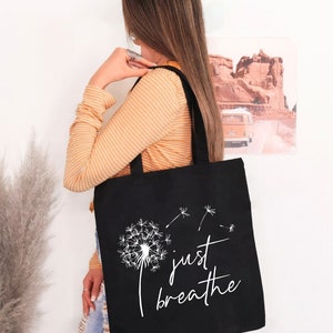 May include: Black tote bag with a white dandelion design and the text "just breathe".