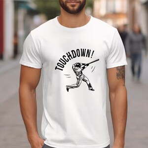 May include: White t-shirt with a black graphic of a baseball player running with a bat and the text "TOUCHDOWN!"