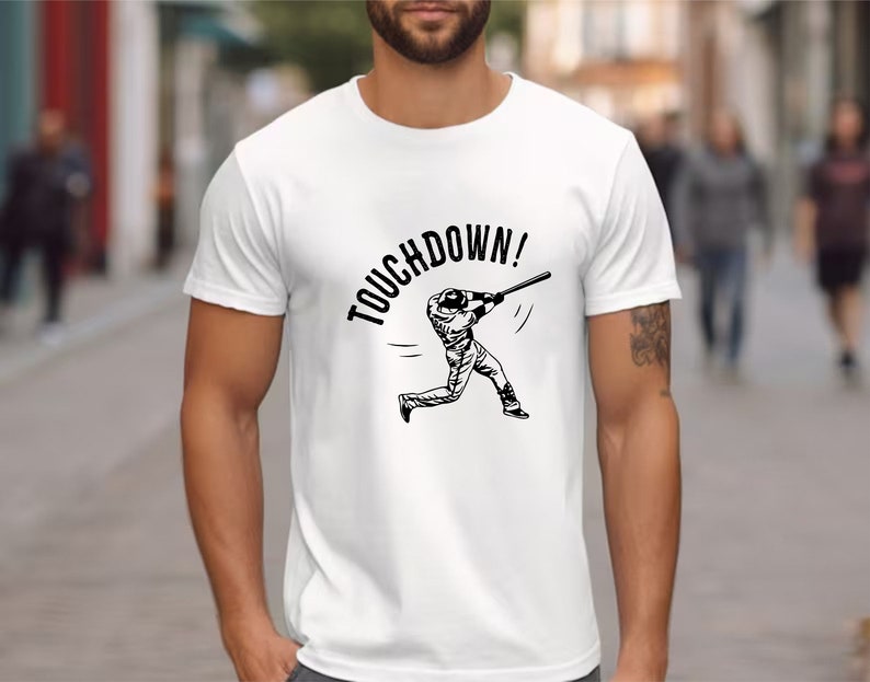 May include: White t-shirt with a black graphic of a baseball player running with a bat and the text "TOUCHDOWN!"