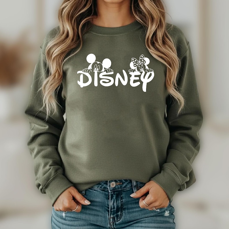 Pu&ograve; includere: Una felpa verde oliva con la scritta "DISNEY" in bianco e grafiche di Topolino e Minnie Mouse sopra le lettere. La felpa a maniche lunghe &egrave; realizzata in un materiale morbido.