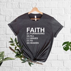 以下が含まれることがあります： 白い文字で「FAITH」とプリントされた濃いグレーのTシャツ。文字は「Forwarding All Issues To Heaven」の頭文字です。