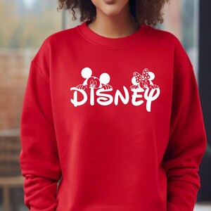Pu&ograve; includere: Una felpa rossa con la scritta bianca "Disney" e grafiche di Topolino e Minnie. La felpa &egrave; di colore rosso pieno.