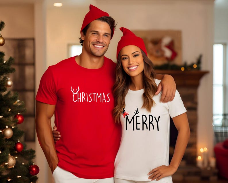 May include: A couple wearing matching red and white Christmas t-shirts and red elf hats. The red shirt says "Christmas" in white script. The white shirt says "Merry" in black script.