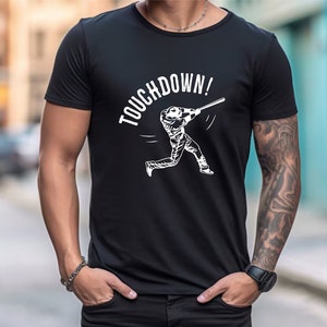 May include: Black t-shirt with a white graphic of a baseball player swinging a bat and the text "TOUCHDOWN!"