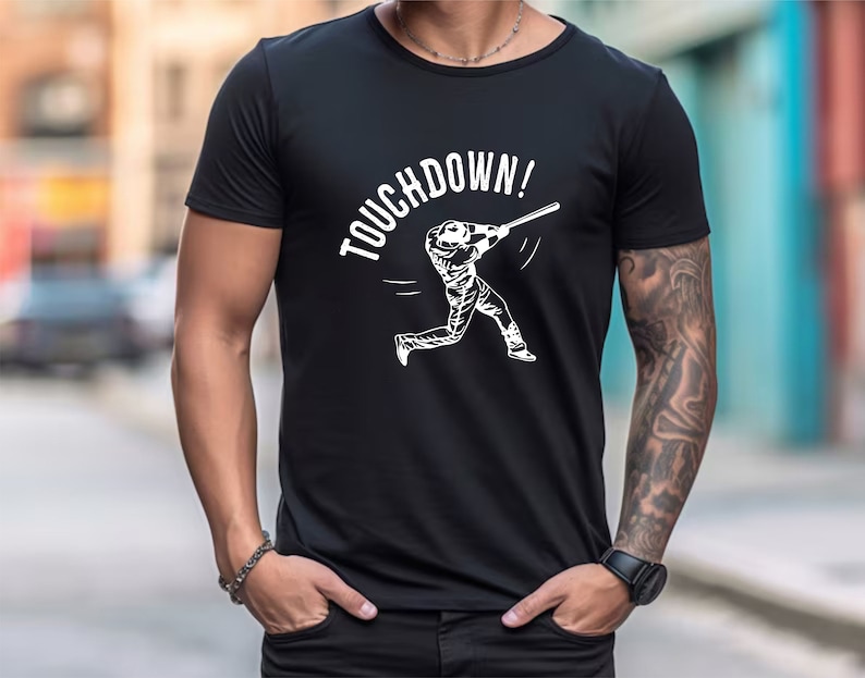 May include: Black t-shirt with a white graphic of a baseball player swinging a bat and the text "TOUCHDOWN!"