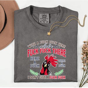 May include: Gray t-shirt with a graphic of a rooster and the text "WITH A FUCK FUCK HERE And a FUCK FUCK THERE HERE A FUCK THERE A FUCK I DON'T GIVE A FUCK FUCK". A gold star pendant necklace is on the shirt.