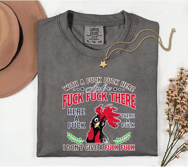 May include: Gray t-shirt with a graphic of a rooster and the text "WITH A FUCK FUCK HERE And a FUCK FUCK THERE HERE A FUCK THERE A FUCK I DON'T GIVE A FUCK FUCK". A gold star pendant necklace is on the shirt.