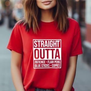 May include: A red t-shirt with the text "STRAIGHT OUTTA" in a white box, followed by "PATIENCE &bull; FLAIR PENS &bull; GLUE STICKS &bull; COPIES" in white. The shirt is short-sleeved.