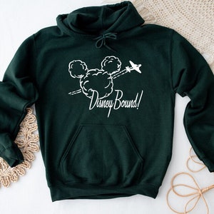 Puede incluir: Una sudadera con capucha verde oscuro con un gr&aacute;fico blanco de la cabeza de Mickey Mouse en nubes con un avi&oacute;n volando por encima. El texto "Disney Bound!" est&aacute; debajo del gr&aacute;fico.