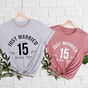 May include: Two t-shirts, one gray and one dusty rose, each with the text "JUST MARRIED 15 Years Ago" in a circular design. The number 15 is in a bold font. Small heart graphics are included.
