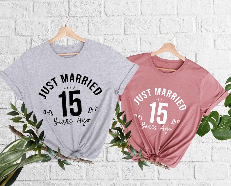 May include: Two t-shirts, one gray and one dusty rose, each with the text "JUST MARRIED 15 Years Ago" in a circular design. The number 15 is in a bold font. Small heart graphics are included.