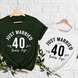 May include: Two short-sleeved t-shirts, one dark green and one white, each displaying the text "JUST MARRIED 40 Years Ago" in a circular design. The number 40 is prominently featured. Small heart graphics are included.