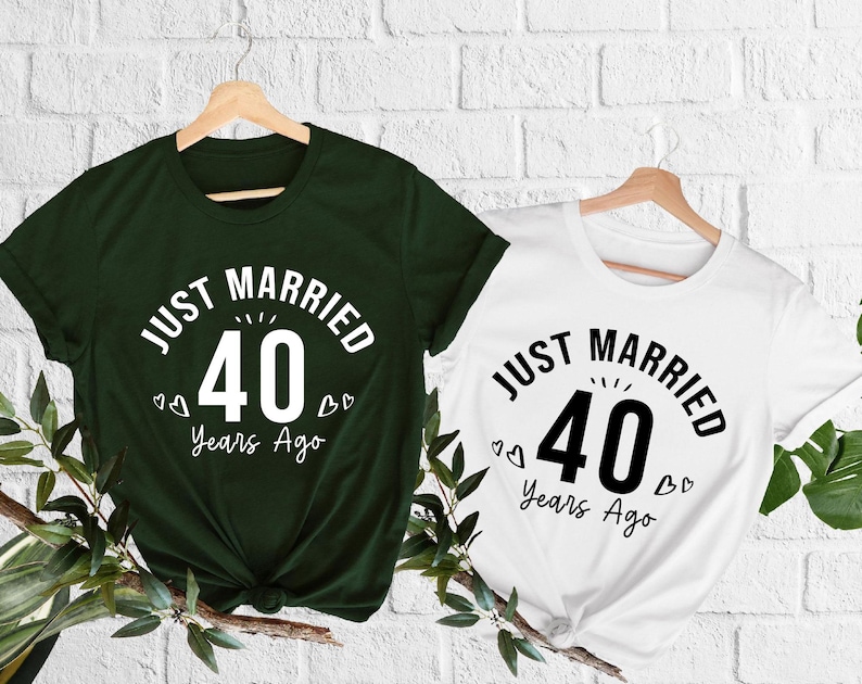 May include: Two short-sleeved t-shirts, one dark green and one white, each displaying the text "JUST MARRIED 40 Years Ago" in a circular design. The number 40 is prominently featured. Small heart graphics are included.