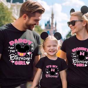 Puede incluir: Familia con camisetas negras a juego con dise&ntilde;os de Mickey Mouse. Las camisetas dicen "Daddy of the Birthday Girl", "Mommy of the Birthday Girl" e "It's My Birthday!" en texto rosa y blanco. Todos llevan orejas de rat&oacute;n.