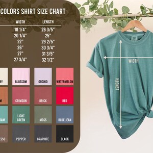 May include: A teal Comfort Colors t-shirt hanging on a wooden hanger, with a size chart and color swatches to the left. The size chart shows measurements in inches for width and length. Colors include white, ivory, and black.
