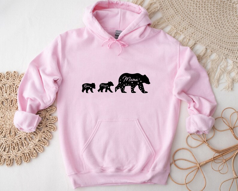 May include: Pink hooded sweatshirt with a black silhouette of three bears. The largest bear says "Mama" and the two smaller bears say "Ryan" and "Mason".