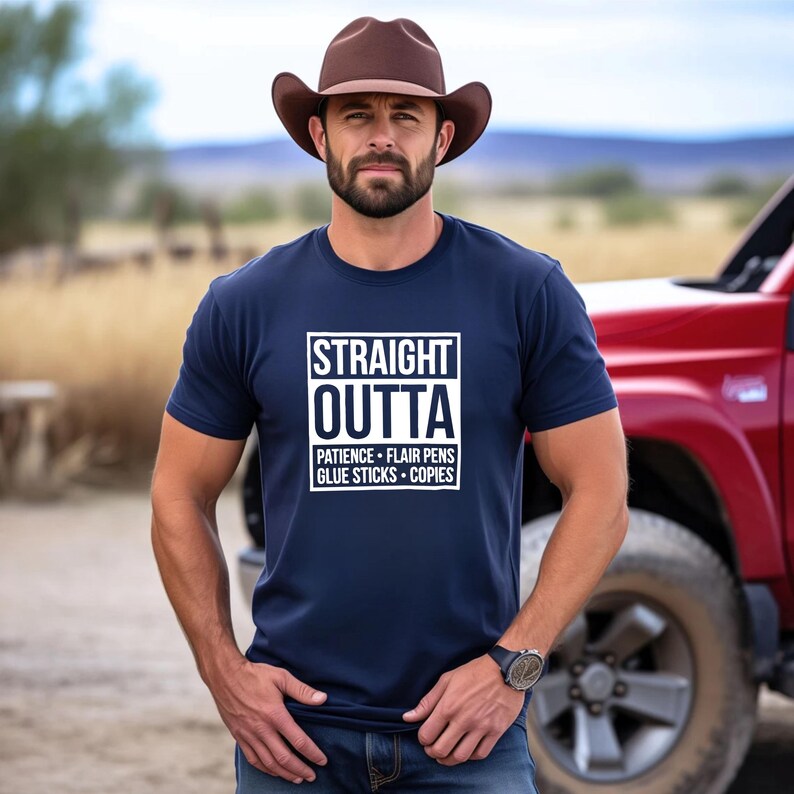 May include: Navy blue t-shirt with the text "STRAIGHT OUTTA" in a white box, followed by "PATIENCE &bull; FLAIR PENS &bull; GLUE STICKS &bull; COPIES". The person is wearing a brown cowboy hat and a watch.