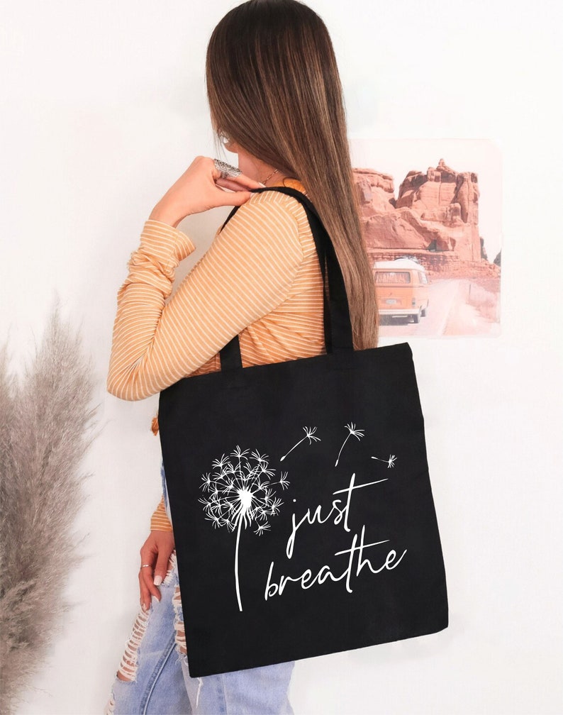 May include: Black tote bag with a white dandelion design and the text "just breathe".