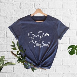 Peut inclure: Un t-shirt bleu marine avec un motif blanc de t&ecirc;te de Mickey Mouse fait de nuages et un petit avion volant au-dessus. Le texte "Disney Bound!" est imprim&eacute; sous le motif.