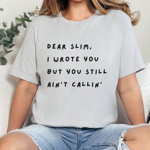 May include: A light gray t-shirt with the text "Dear Slim, I wrote you but you still ain't callin'" printed in black.