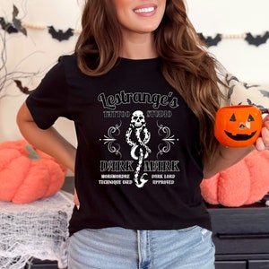 May include: Black t-shirt with a white graphic. The design includes the text "Lestrange's Tattoo Studio" and a Dark Mark design with a skull and snake. The shirt also has the text "Morsmordre Technique Used" and "Dark Lord Approved".