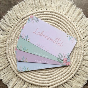 May include: Four cards with floral designs and the text "Lebensmittel" and "oh budgit - oh yes" on a beige crocheted round mat with fringe.