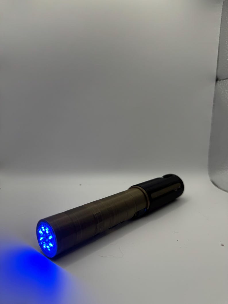 May include: A cylindrical flashlight with a bronze-colored body and a black head. The flashlight emits a bright blue light from the front, illuminating the surrounding area. The light source is composed of multiple small LEDs.