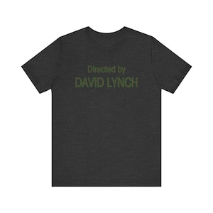 Puede incluir: Camiseta gris oscuro jaspeada con el texto "Directed by DAVID LYNCH" en verde.