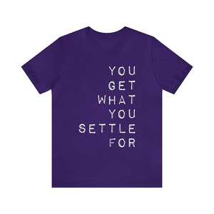 May include: Purple t-shirt with the text "YOU GET WHAT YOU SETTLE FOR" printed in white.