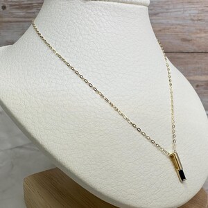 May include: A gold chain necklace with a black rectangular pendant. The pendant is set in a gold frame.