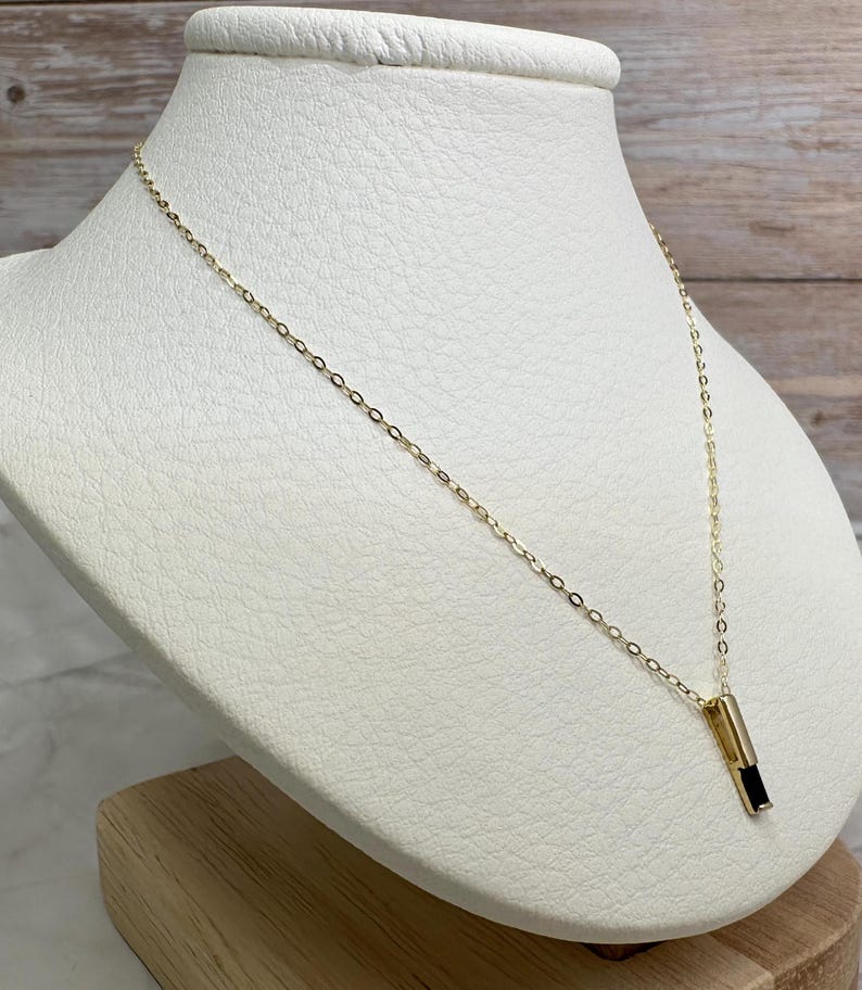 May include: A gold chain necklace with a black rectangular pendant. The pendant is set in a gold frame.