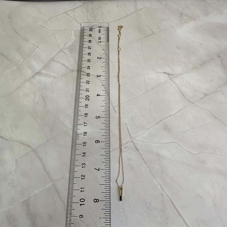 May include: A gold chain necklace with a small black stone pendant. The necklace is about 18 inches long.