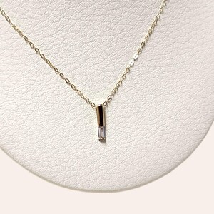 May include: A delicate gold chain necklace with a small, clear, rectangular pendant.