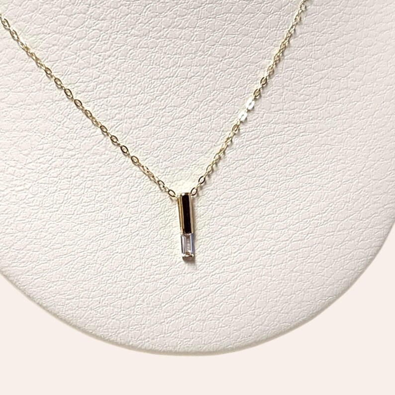 May include: A delicate gold chain necklace with a small, clear, rectangular pendant.