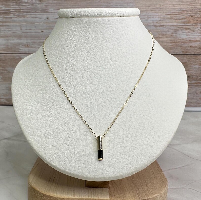 May include: A gold chain necklace with a black rectangular pendant.