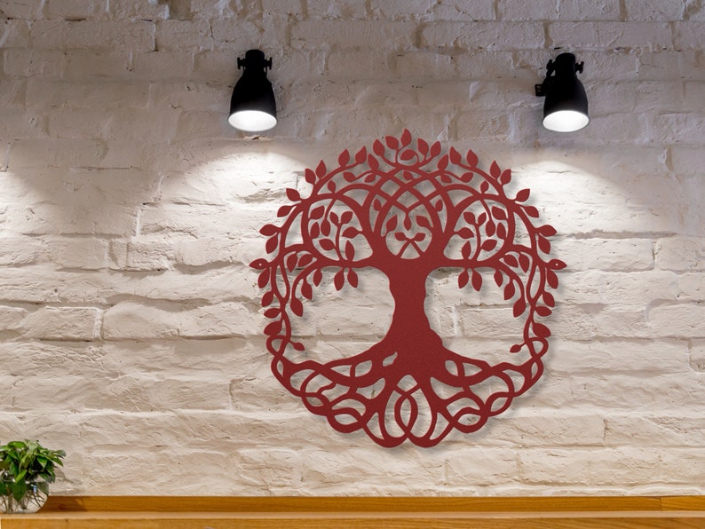 May include: A red wooden tree of life wall decor with intricate details and a circular shape. The tree is mounted on a white brick wall with two black wall lights on either side.