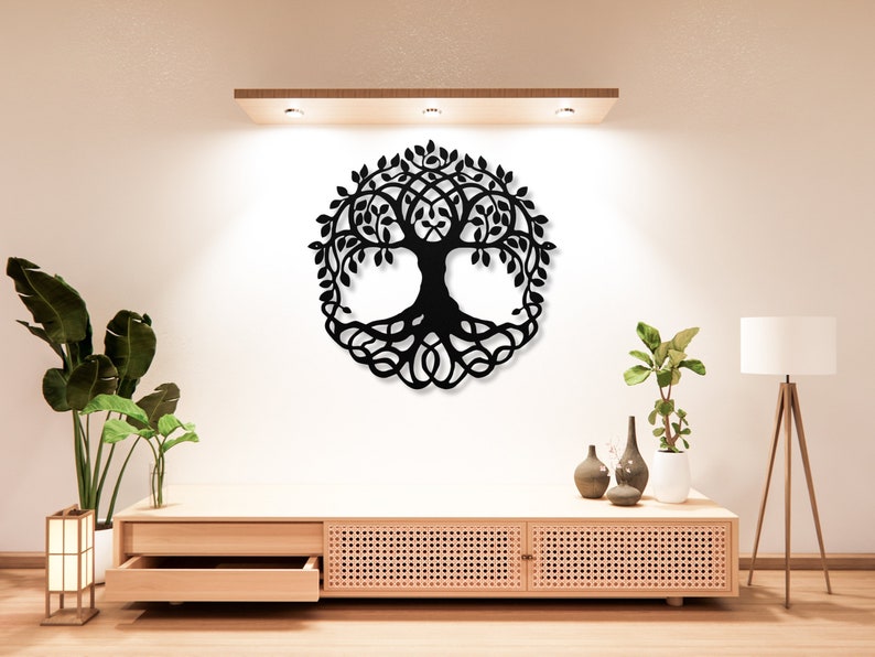 May include: Black metal wall art featuring a tree of life design. The tree has intricate branches and roots, and is enclosed within a circle. The art is mounted on a white wall above a wooden shelf with plants and decorative items.