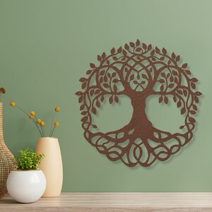 May include: A brown wooden wall decoration in the shape of a tree of life with intricate details. The tree is surrounded by leaves and has a thick trunk and roots. The decoration is hanging on a green wall.