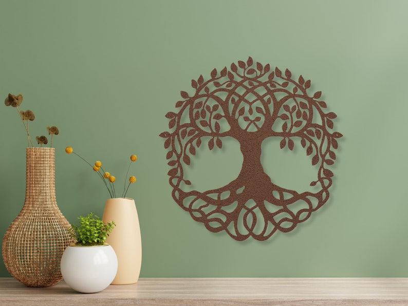 May include: A brown wooden wall decoration in the shape of a tree of life with intricate details. The tree is surrounded by leaves and has a thick trunk and roots. The decoration is hanging on a green wall.