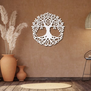 May include: White wooden wall decor in the shape of a tree of life with intricate branches and roots. The decor is hanging on a brown wall with a vase of dried pampas grass and a black metal stool in the foreground.