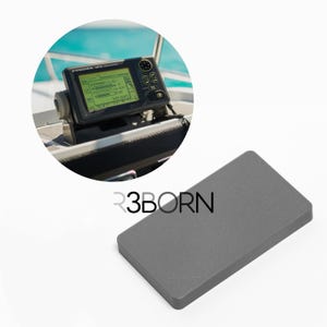 May include: A marine GPS navigation system with a screen displaying data, mounted on a boat's console. A grey rectangular object is in the foreground, with the text "R3BORN" printed on it.