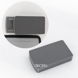 May include: A gray rectangular cover with rounded edges, possibly for a marine device. The cover is shown in two views, one in place and another detached. The text "R3BORN" is visible on the lower right corner.