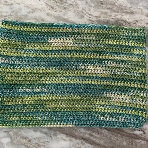 May include: A crocheted clutch bag in shades of green, blue, and white. The bag has a textured, woven pattern.