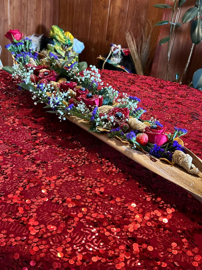 K&ouml;nnte beinhalten: Ein langes Holztablett gef&uuml;llt mit roten Rosen, Blaubeeren und anderen getrockneten Fr&uuml;chten und Blumen. Das Tablett steht auf einer roten, paillettenbesetzten Tischdecke.