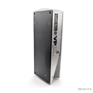 Peut inclure: Pédale de volume Ernie Ball VP Jr. argent et noir. La pédale a une base rectangulaire noire avec des vis dorées et un dessus argenté incliné avec le texte "Ernie Ball VP Jr." en noir. Sur fond blanc.