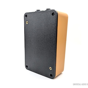 May include: A black and tan colored metal box with a textured surface. The box has a Universal Audio Double logo on the side.