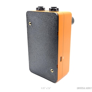 May include: An orange and black audio device with two black knobs on top. The device has a textured black front panel and is labeled "UNIVERSAL AUDIO SINGLE". It measures 4.45" x 2.6".