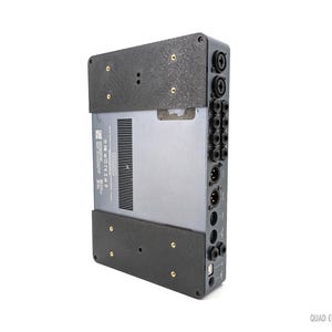 May include: Black audio interface with multiple ports and a black and gray textured panel. The text "QUAD CORTEX" is printed on the bottom right corner of the panel.