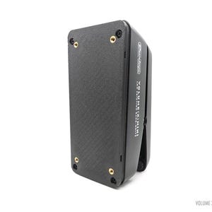 May include: A black Dunlop Volume X Mini pedal with a textured surface and gold-colored screws. The pedal has the text "VOLUME X MINI" and "LEV FRICTION BAND DRIVE" printed on the side. The pedal is on a white background.