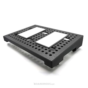 May include: A black plastic stand with a perforated surface and two white rectangular inserts. The stand has four small feet on the bottom.